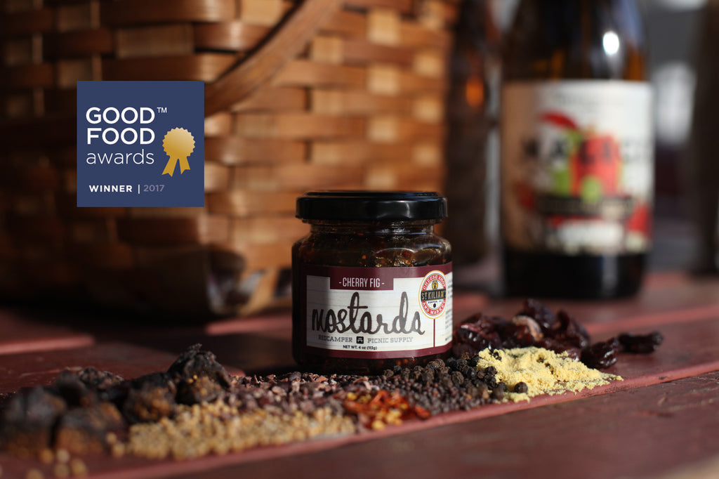 Small jar of RedCamper Cherry Fig Mostarda surrounded by spices mustard seeds, red pepper flakes, cocoa nibs, black pepper